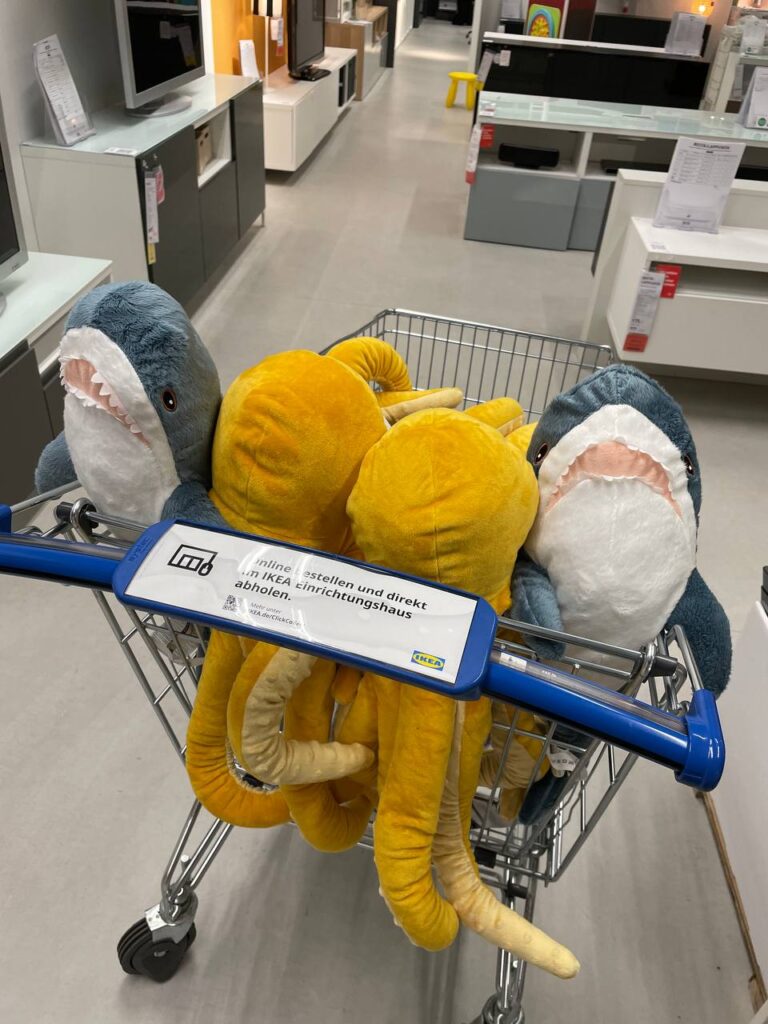 Im Kindersitz eines Ikea-Einkaufswagens sitzen 4 Plüschtiere: 2 Mini-Haie und zwei Oktopoden.