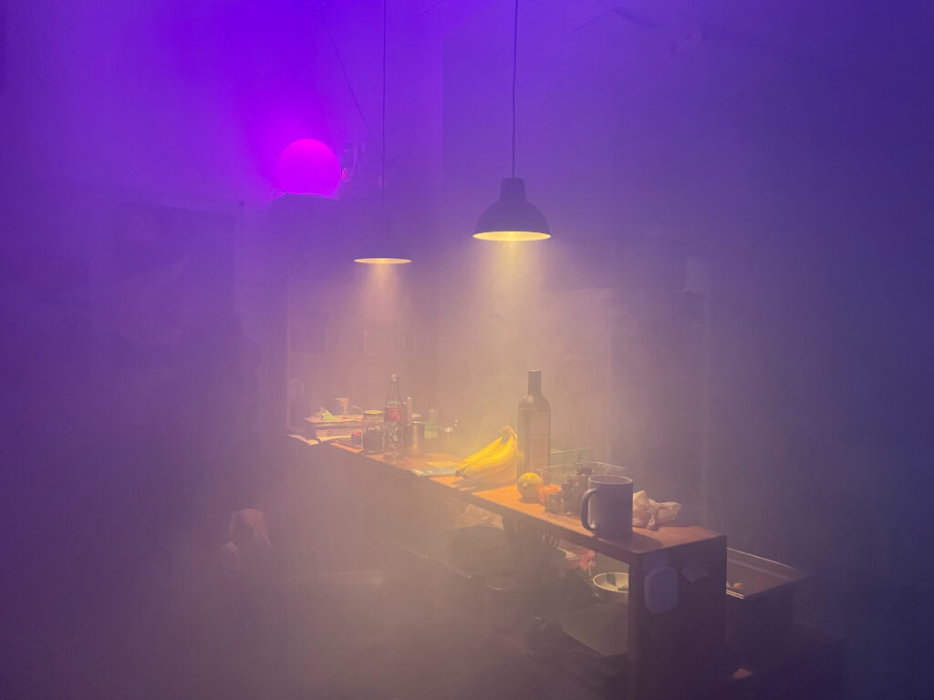 Die Bar in der Lounge ist komplett in Nebel eingehüllt. Die Hängeleuchten über dem Tresen und eine runde RGB-Leuchte im Hintergrund leuchten sanft.