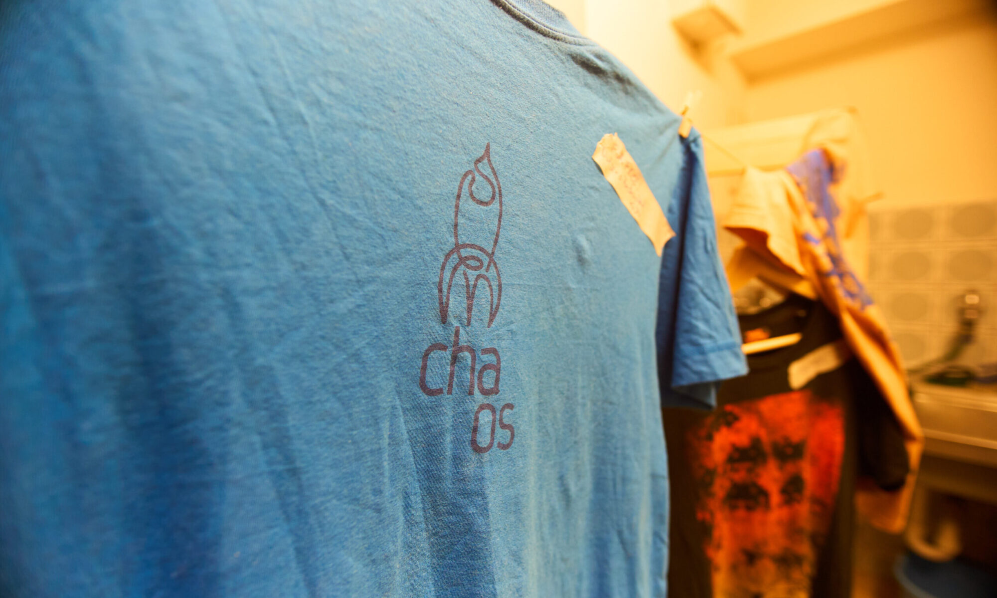 A blue t-shirt with a fairydust rocket and the text "chaos" hanging from a washing line.