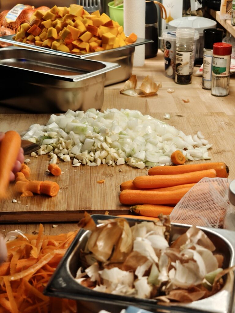 Geschnittene und geschälte Karotten und Zwiebeln auf einem Schnittbrett in der Küche.